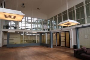 Open en licht kantoorinterieur aan het Gedempt Hamerkanaal met glazen wanden, houten vloer en industriële verlichting.